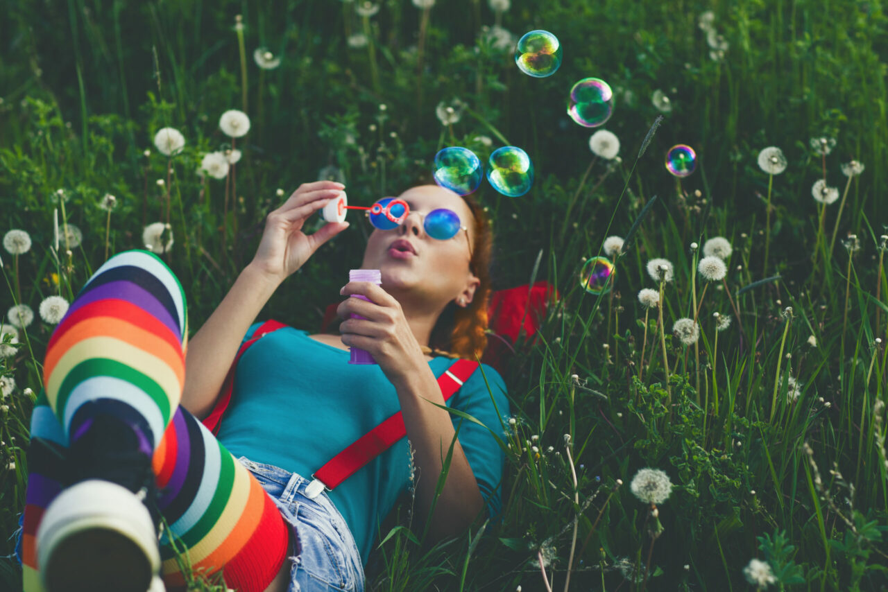 Young girl smiling with her hands up beside her looking up at the sky sitting in a feild of orange flowers